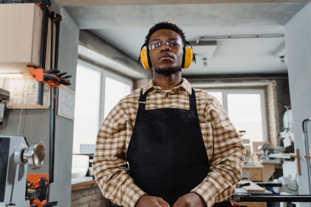 A carpenter standing in a workshop wearing safety glasses and ear protection